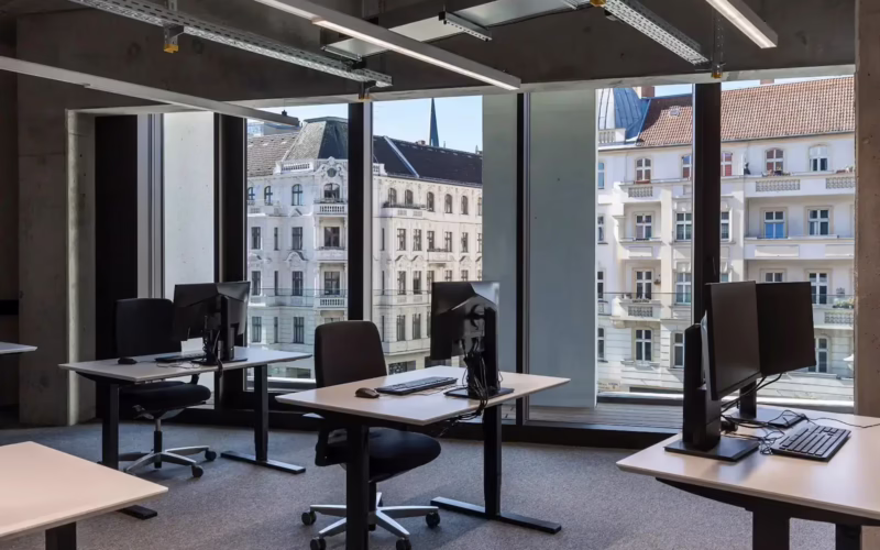 KiezBüro office with desks and monitors by large windows