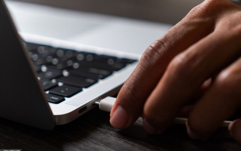 Hand plugging a cable into the side of a laptop
